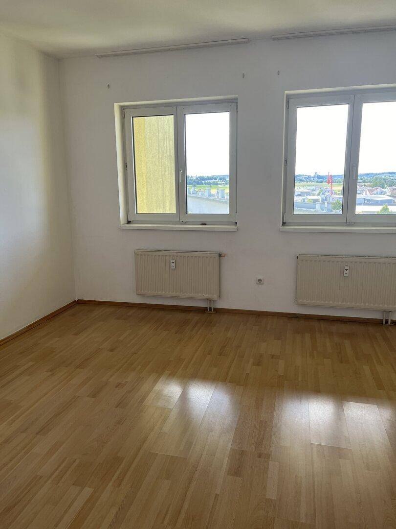 Geräumiges Zimmer mit Parkettboden, großen Fenstern und einem weiten Fernblick über die Umgebung.