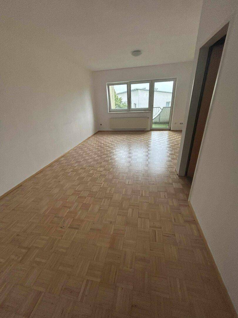 Helles Wohnzimmer mit Parkettboden und Zugang zu einem kleinen Balkon oder einer Terrasse.