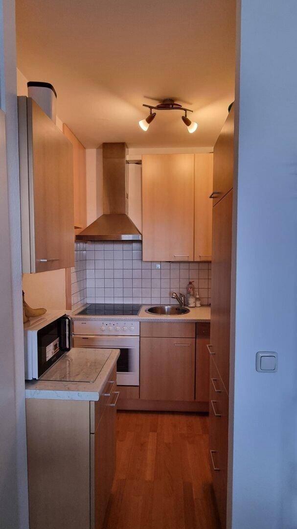 Kleine Einbauküche mit hellen Holzschränken, Fliesenrückwand und integrierten Geräten.