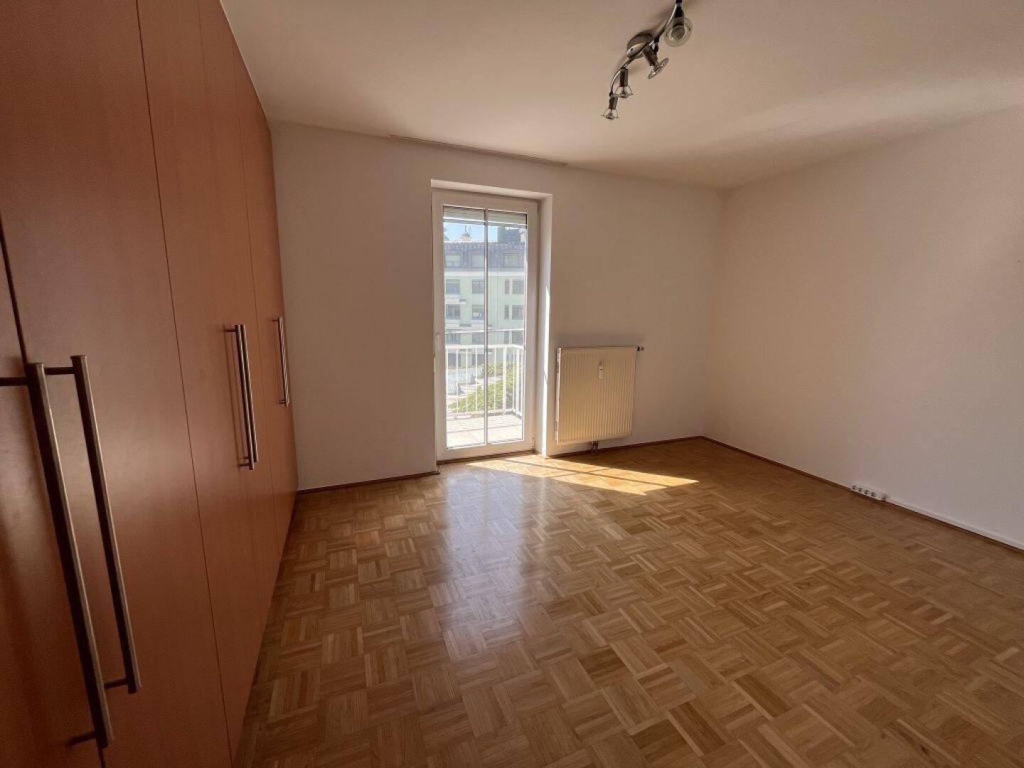 Leeres Schlafzimmer mit Parkettboden, großem Kleiderschrank und Zugang zu einem französischen Balkon.