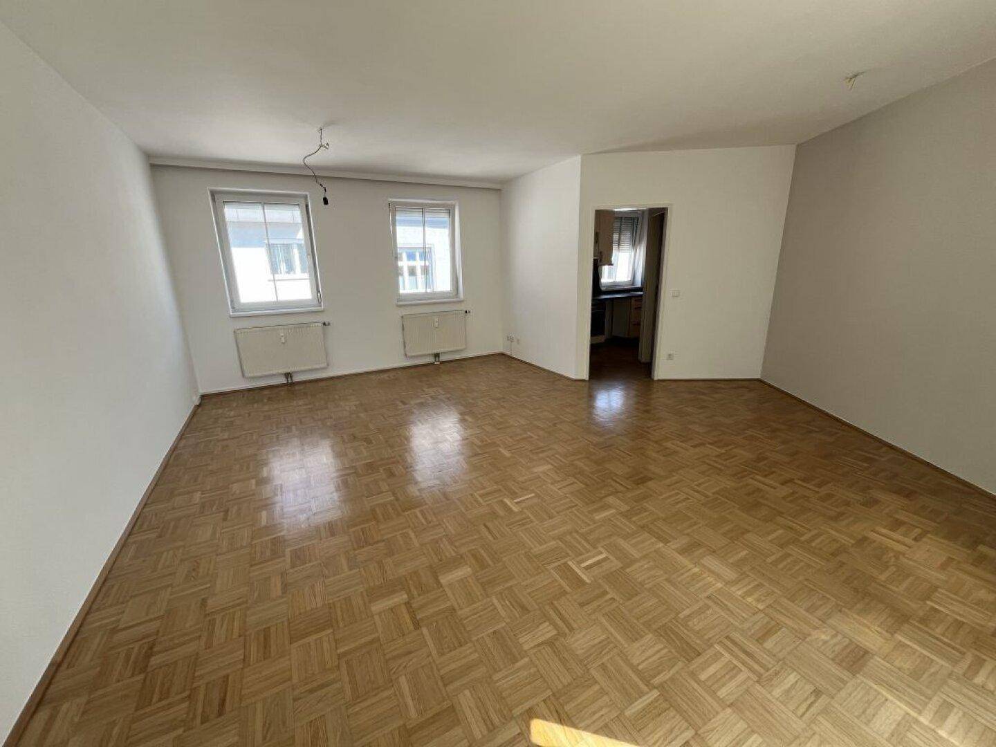 Geräumiges leeres Wohnzimmer mit Parkettboden und zwei Fenstern, bereit zur individuellen Gestaltung.