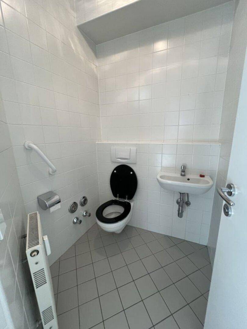Kleines Gäste-WC mit Wand-WC, Handwaschbecken und Haltegriff für Barrierefreiheit.
