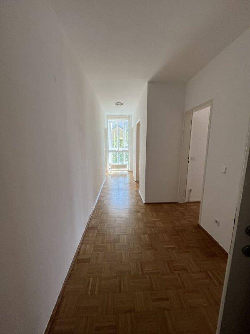 Langer, heller Flur mit Parkettboden und Fenstern am Ende, der zu weiteren Räumen führt.