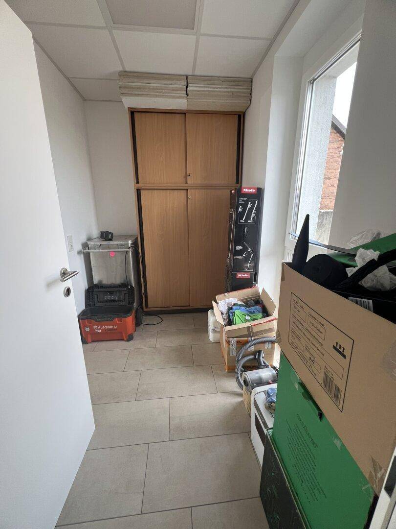 Abstellraum oder Flur mit Schränken und verschiedenen Gegenständen, gut beleuchtet durch ein Fenster.