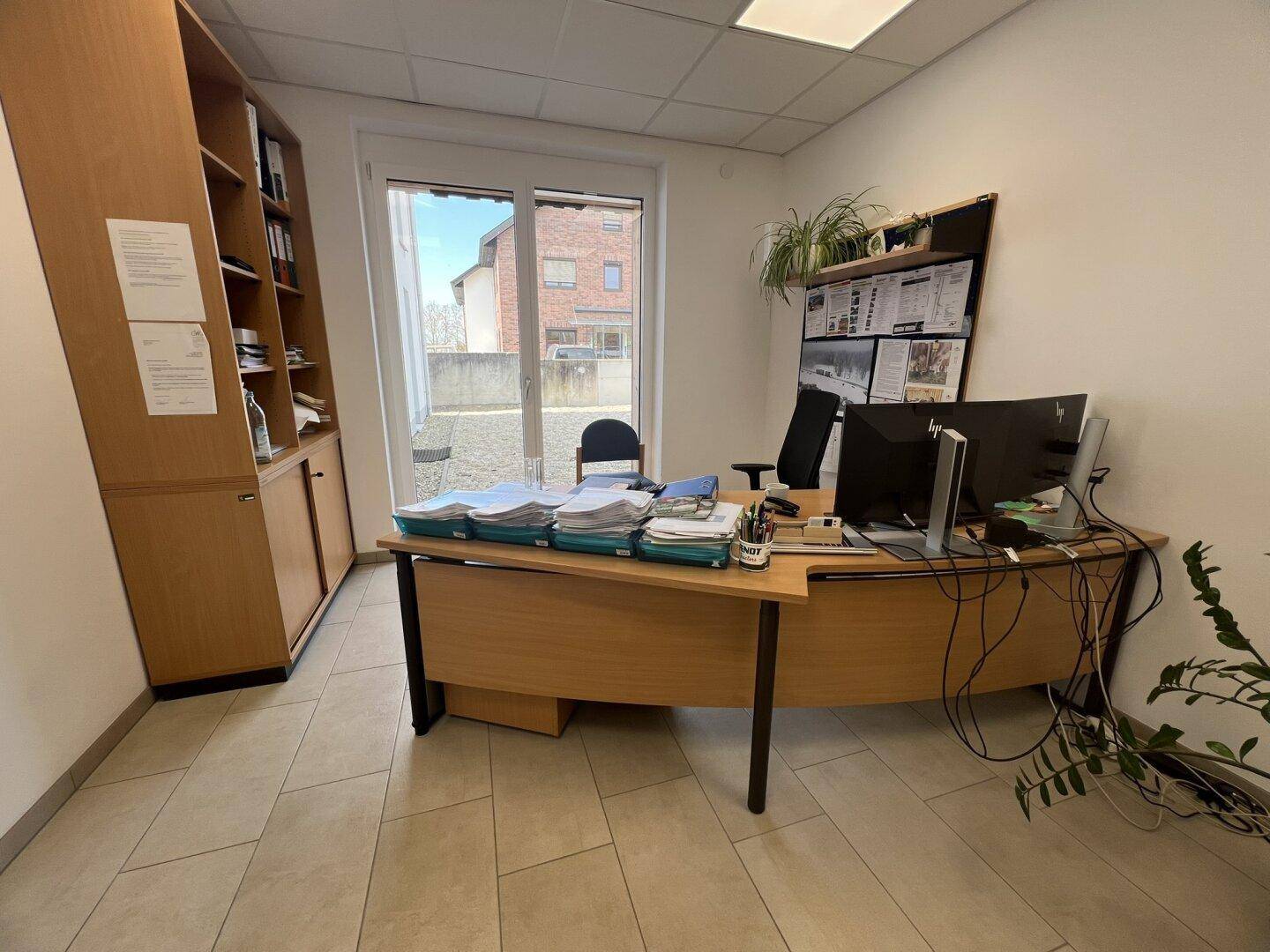 Büro mit großem Schreibtisch, Holzregal und Zugang zu einem Außenbereich durch eine Glastür.