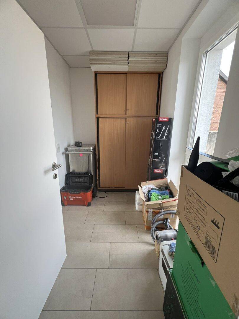 Abstellraum oder Flur mit Schränken und verschiedenen Gegenständen, gut beleuchtet durch ein Fenster.