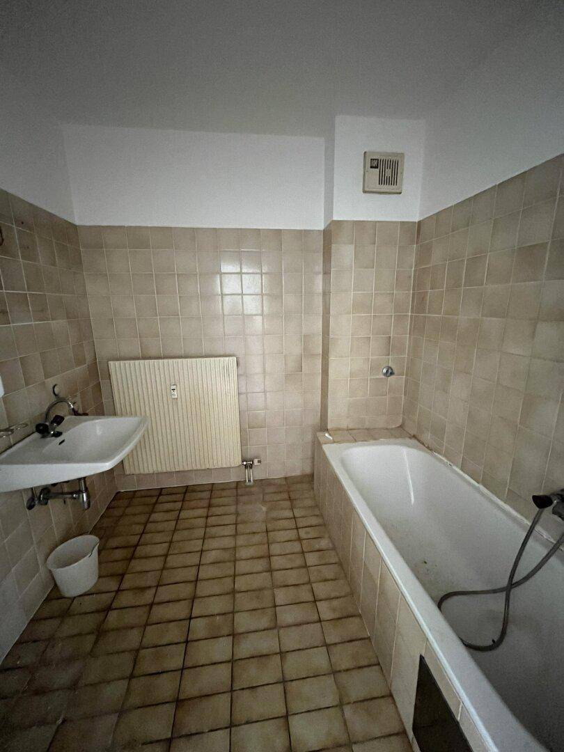 Badezimmer mit beigefarbenen Fliesen, Badewanne und Waschbecken im 80er-Jahre-Stil.