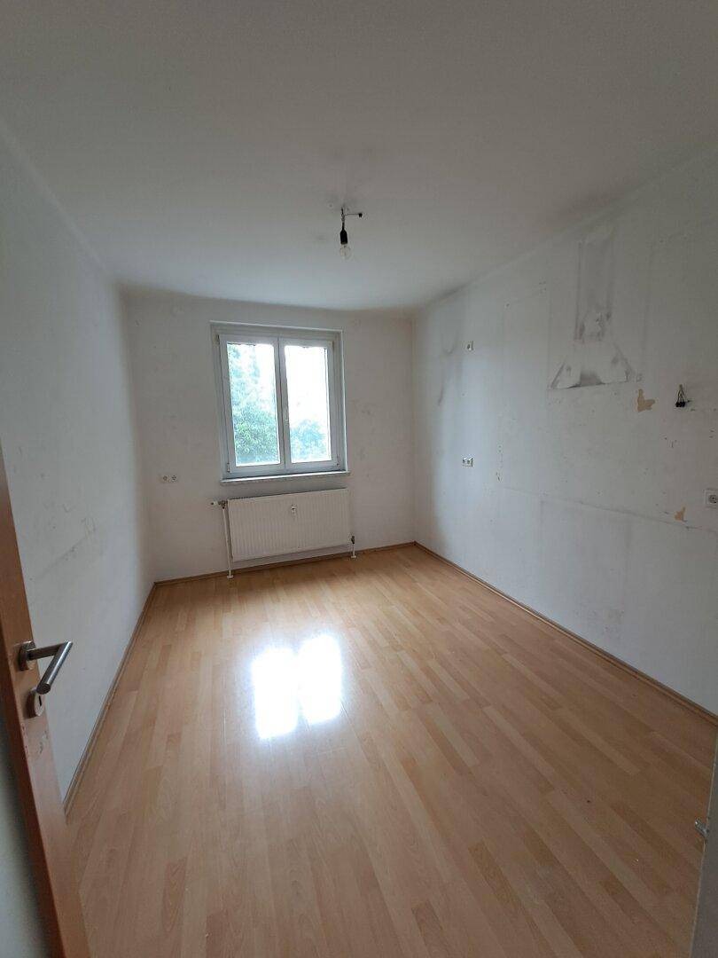 Leeres Zimmer mit Laminatboden und einem Fenster, bereit zur individuellen Gestaltung.