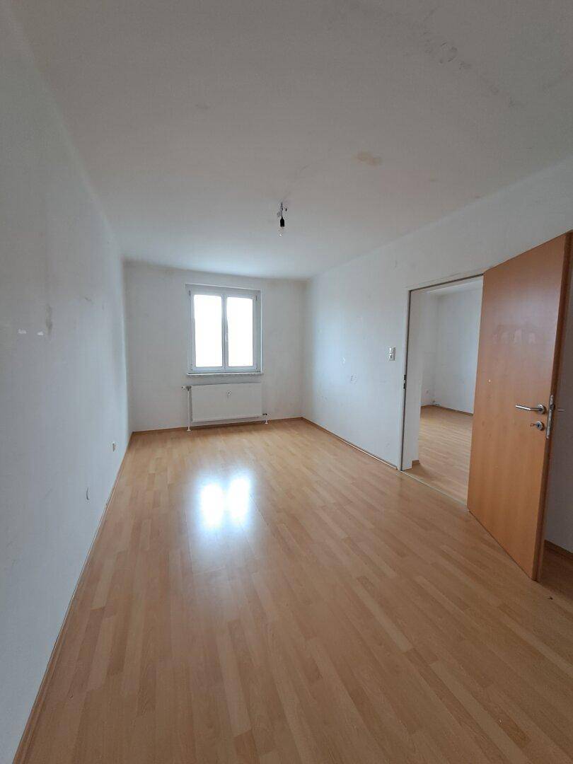 Heller, leerer Raum mit Laminatboden und einem Fenster, ideal für Wohn- oder Schlafbereich.