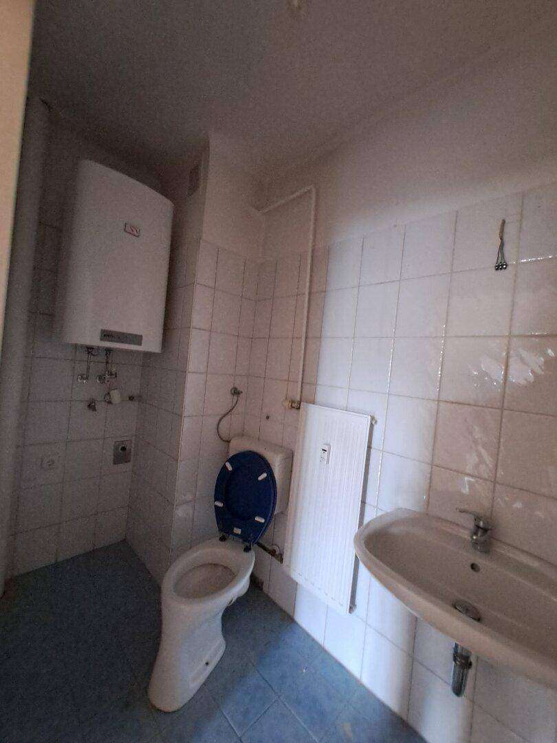 Kleines Badezimmer mit Toilette, Waschbecken und Wandboiler, gefliest in Weiß und Blau.