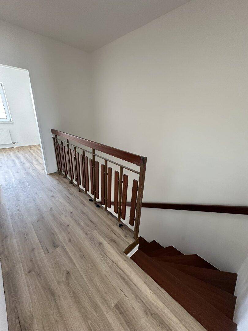 Heller Flur mit Laminatboden und einer Holztreppe, die in die untere Etage führt.