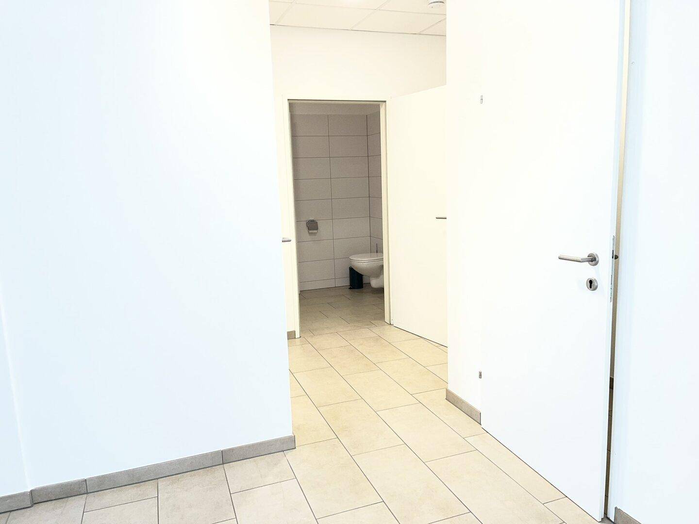 Flur mit hellen Fliesen und Zugang zu einem Badezimmer, wirkt sauber und funktional.