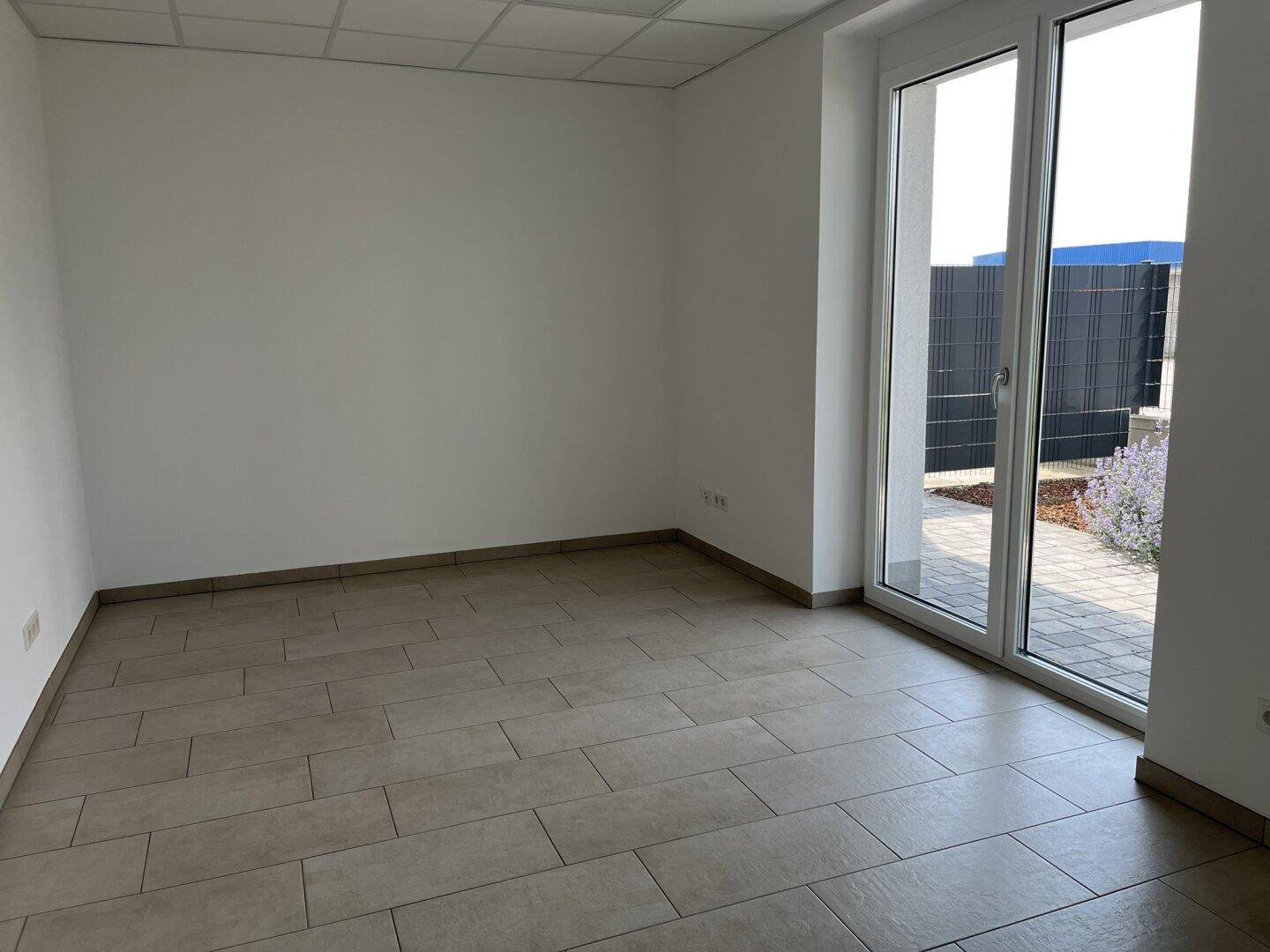 Heller Büroraum mit großen Fenstern und neutralen Fliesen, bietet Zugang zum Außenbereich.