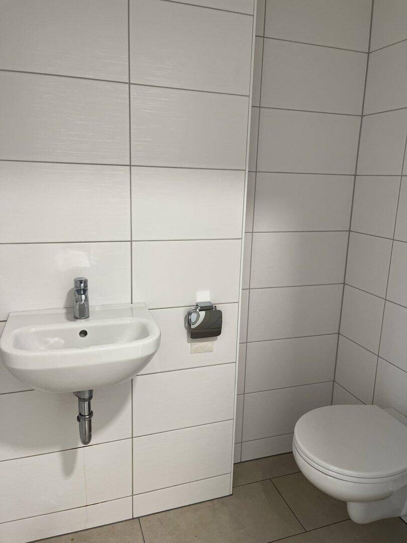 Modernes Gäste-WC mit weißen Fliesen, wandhängendem WC und kleinem Waschbecken.
