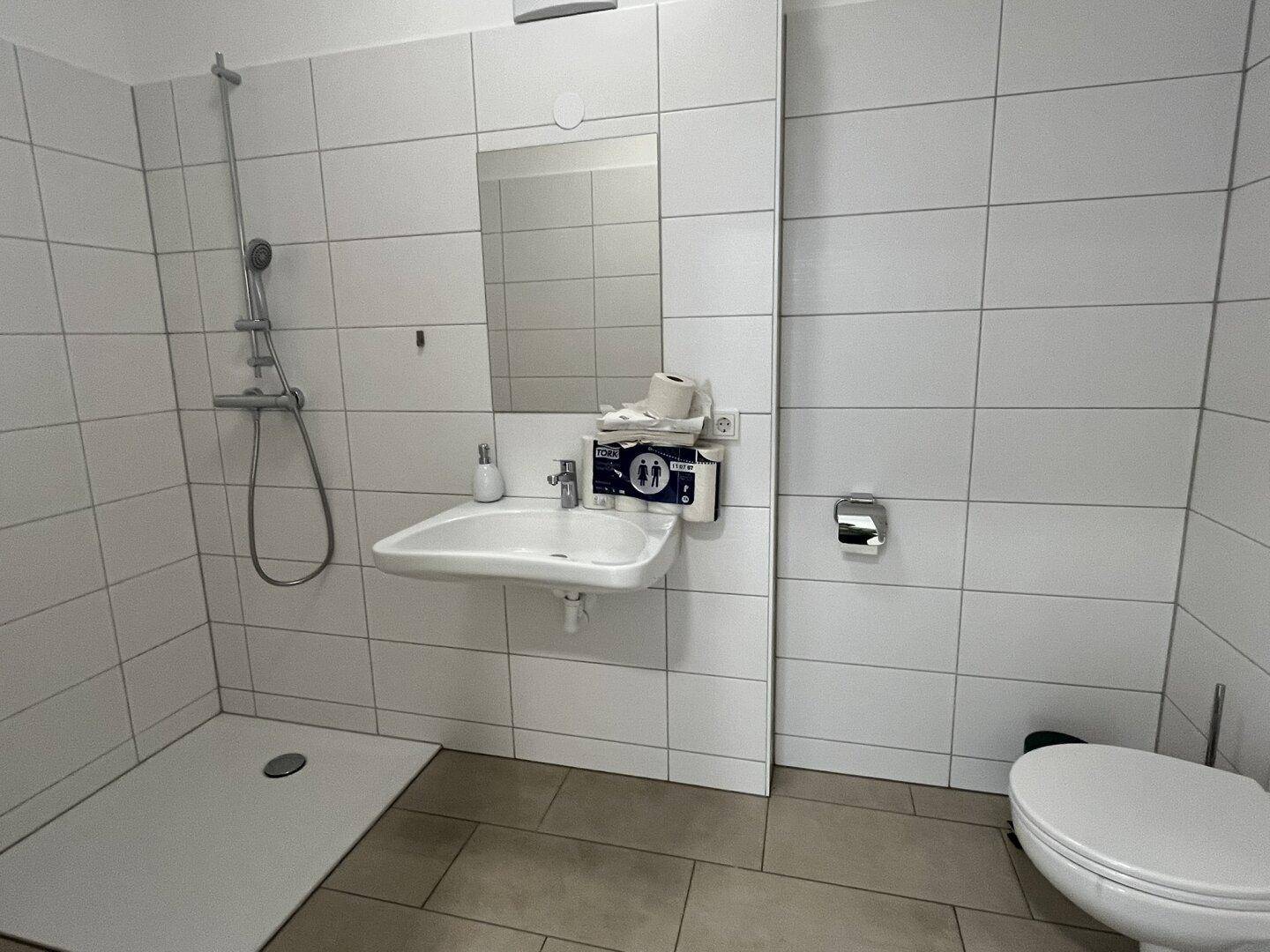 Barrierefreies Badezimmer mit ebenerdiger Dusche, wandhängendem WC und großem Spiegel.