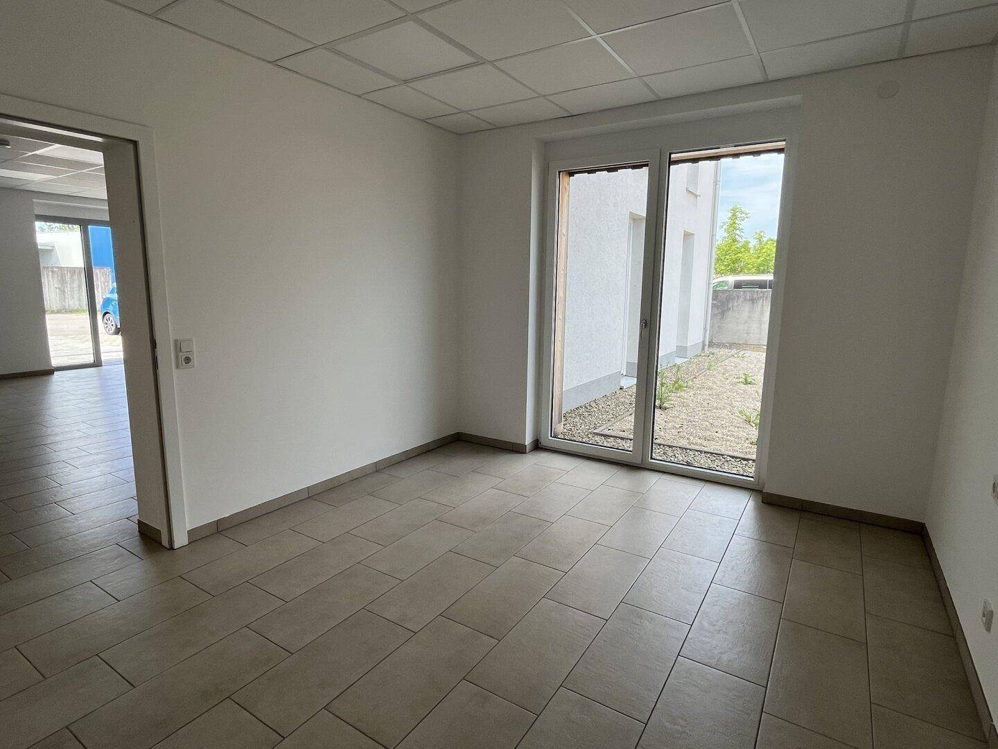 Büroraum mit Zugang zum Außenbereich und Blick auf die Umgebung, ausgestattet mit Fliesenboden.