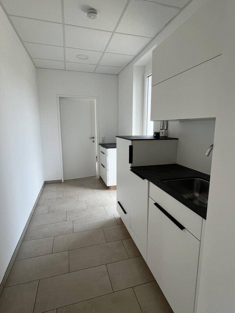 Moderne Küchenzeile mit weißen Schränken und dunkler Arbeitsplatte, ideal für kleine Pausenbereiche.