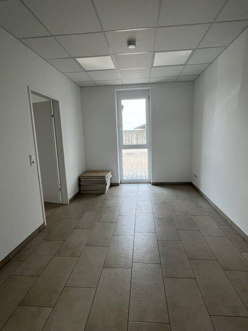 Langer, schmaler Büroraum mit Fenster und Fliesenboden, bietet Platz für individuelle Arbeitsplätze.