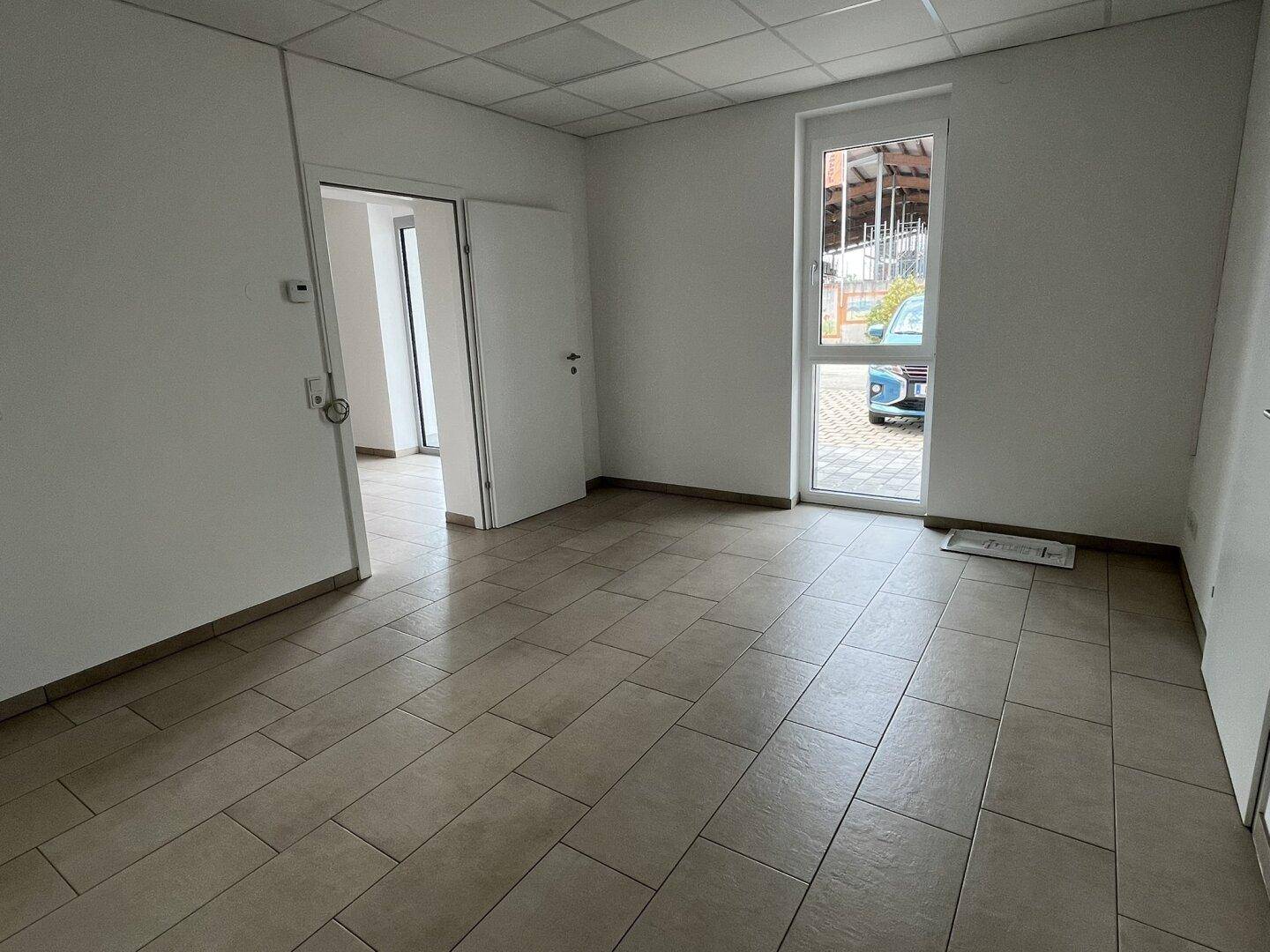 Geräumiger Büroraum mit Fenster und Zugang zu weiteren Bereichen, ideal für flexible Nutzung.