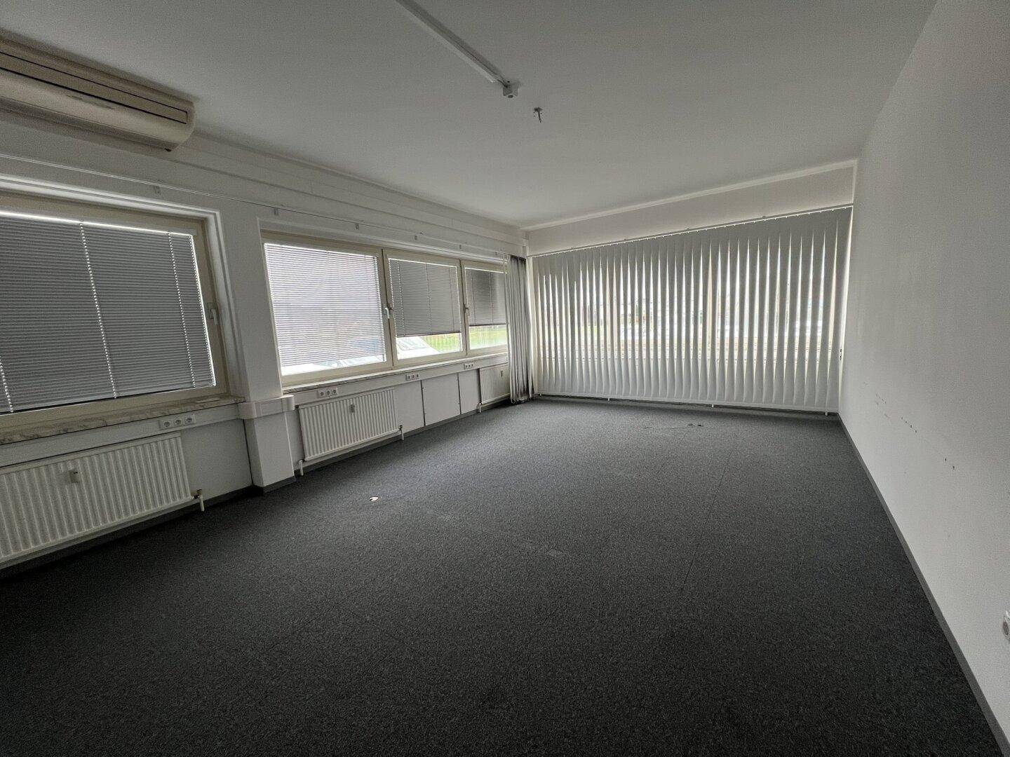 Geräumiges Büro mit Teppichboden, vielen Fenstern und Klimaanlage, bereit zur Nutzung.