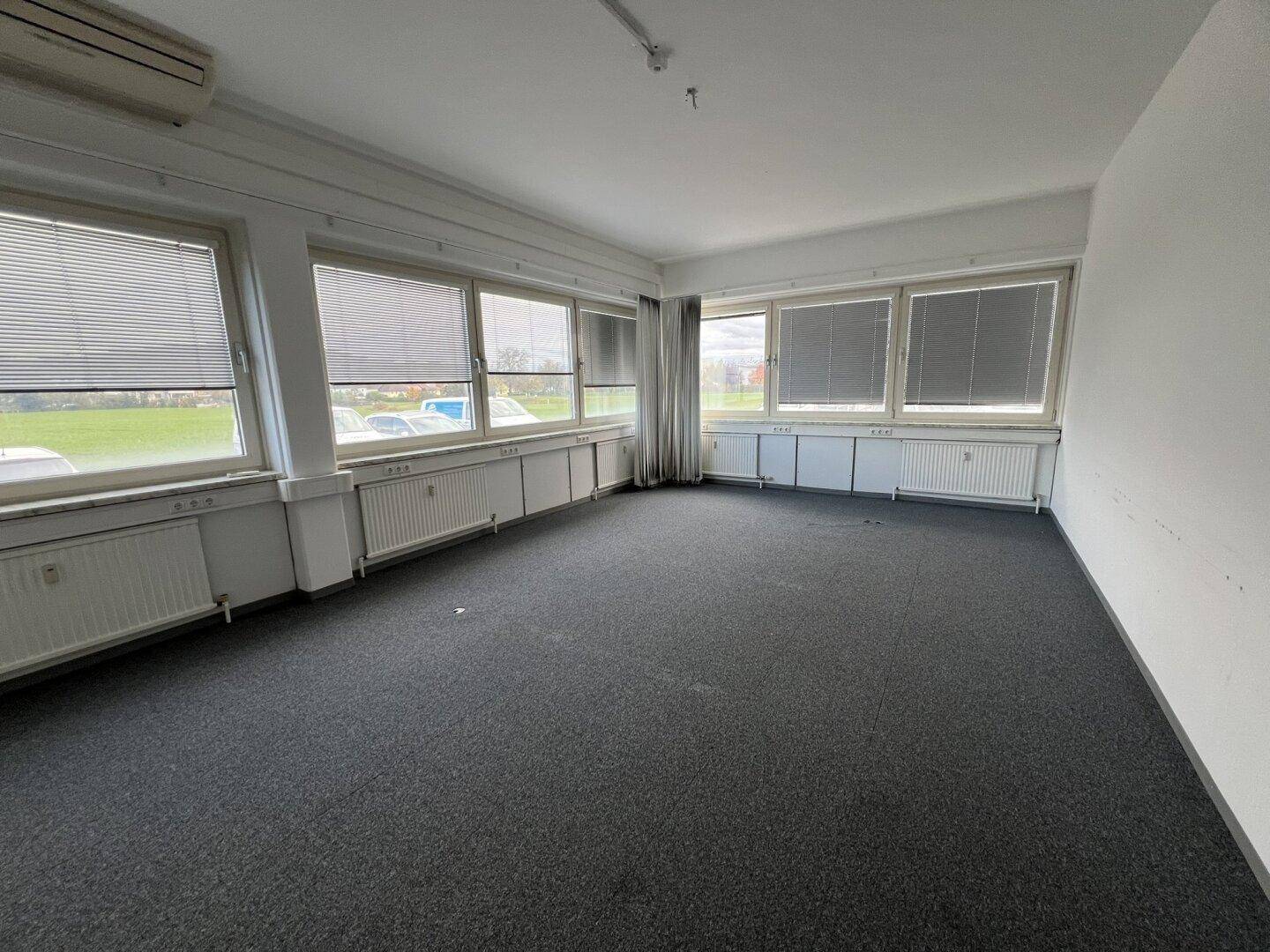 Leeres Büro mit Teppichboden, vielen Fenstern und Blick ins Grüne, inklusive Klimaanlage.
