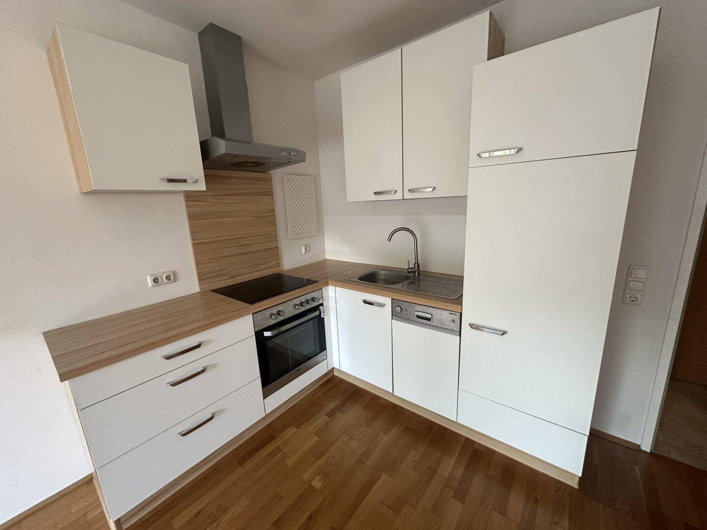 Moderne Einbauküche mit weißen Schränken, Holz-Arbeitsplatte und integrierten Geräten.