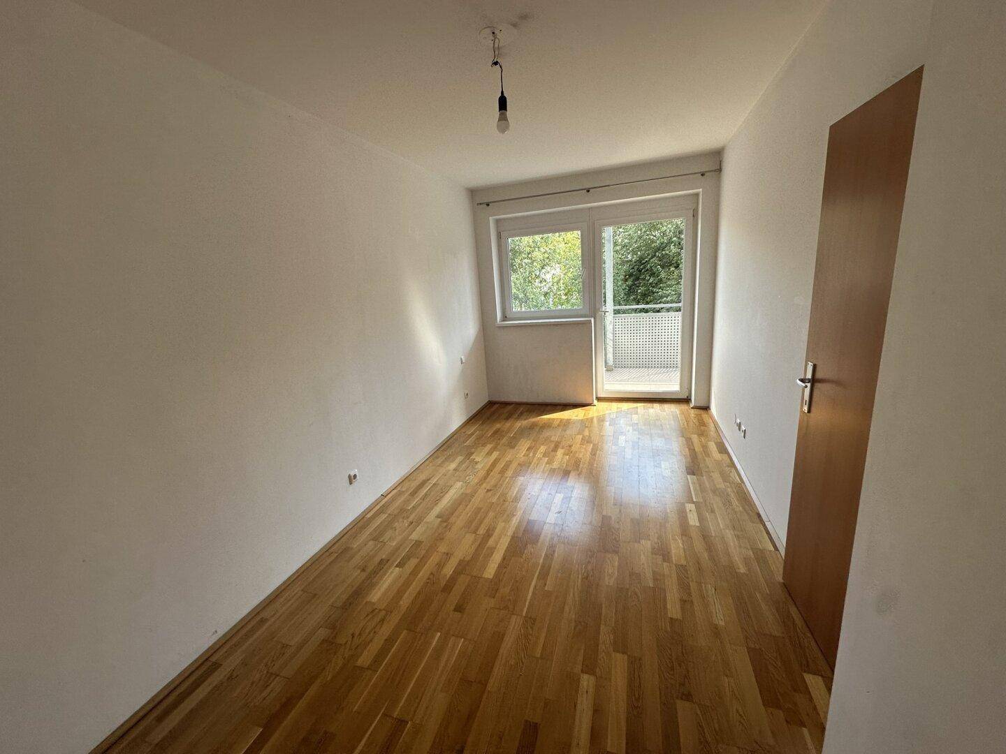 Helles Schlafzimmer mit Parkettboden und direktem Zugang zu einem Balkon.