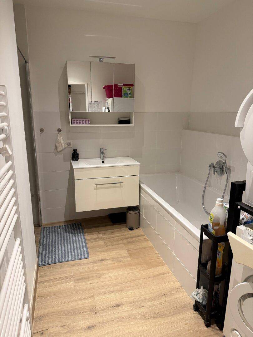 Modernes Badezimmer mit Badewanne, Waschbecken, Spiegelschrank und Handtuchheizkörper.
