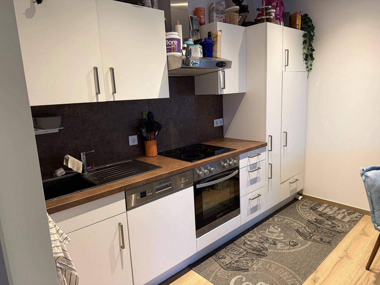 Kompakte Einbauküche mit weißen Schränken, Holz-Arbeitsplatte und modernen Geräten.