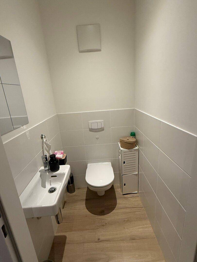 Kleines Gäste-WC mit Wand-WC, Handwaschbecken und halbhohen Fliesen.