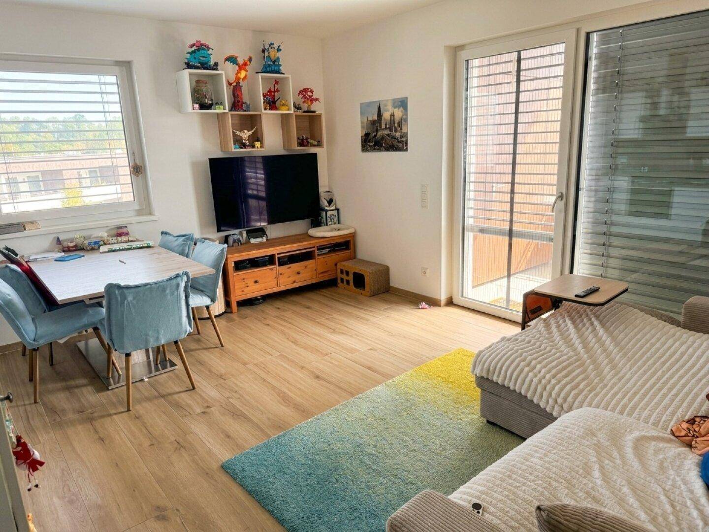 Heller Wohn- und Essbereich mit Laminatboden, Zugang zum Balkon und moderner Dekoration.