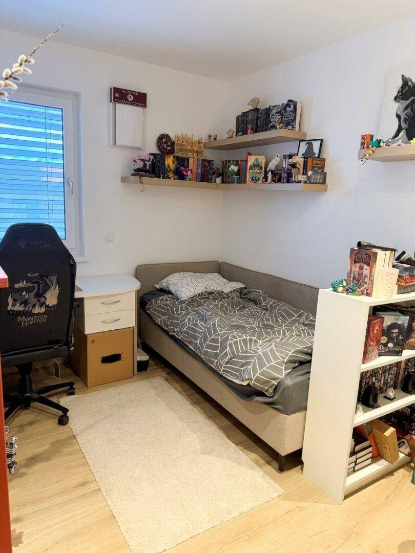 Gemütliches Schlafzimmer mit Einzelbett, Schreibtisch und Wandregalen für persönlichen Stauraum.