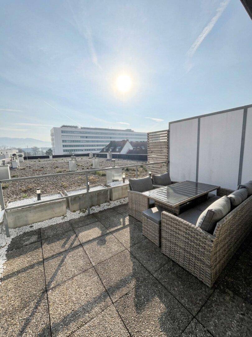 Sonniger Dachterrassenbereich mit Loungemöbeln und weitem Blick über die Stadt.