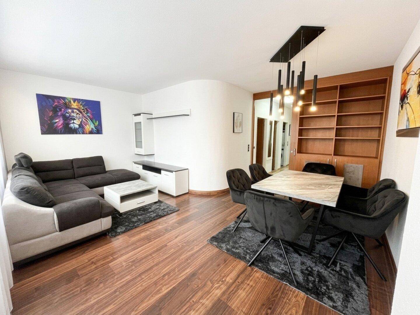 Moderner Wohn-Essbereich mit dunklem Sofa, Esstisch und integriertem Bücherregal.