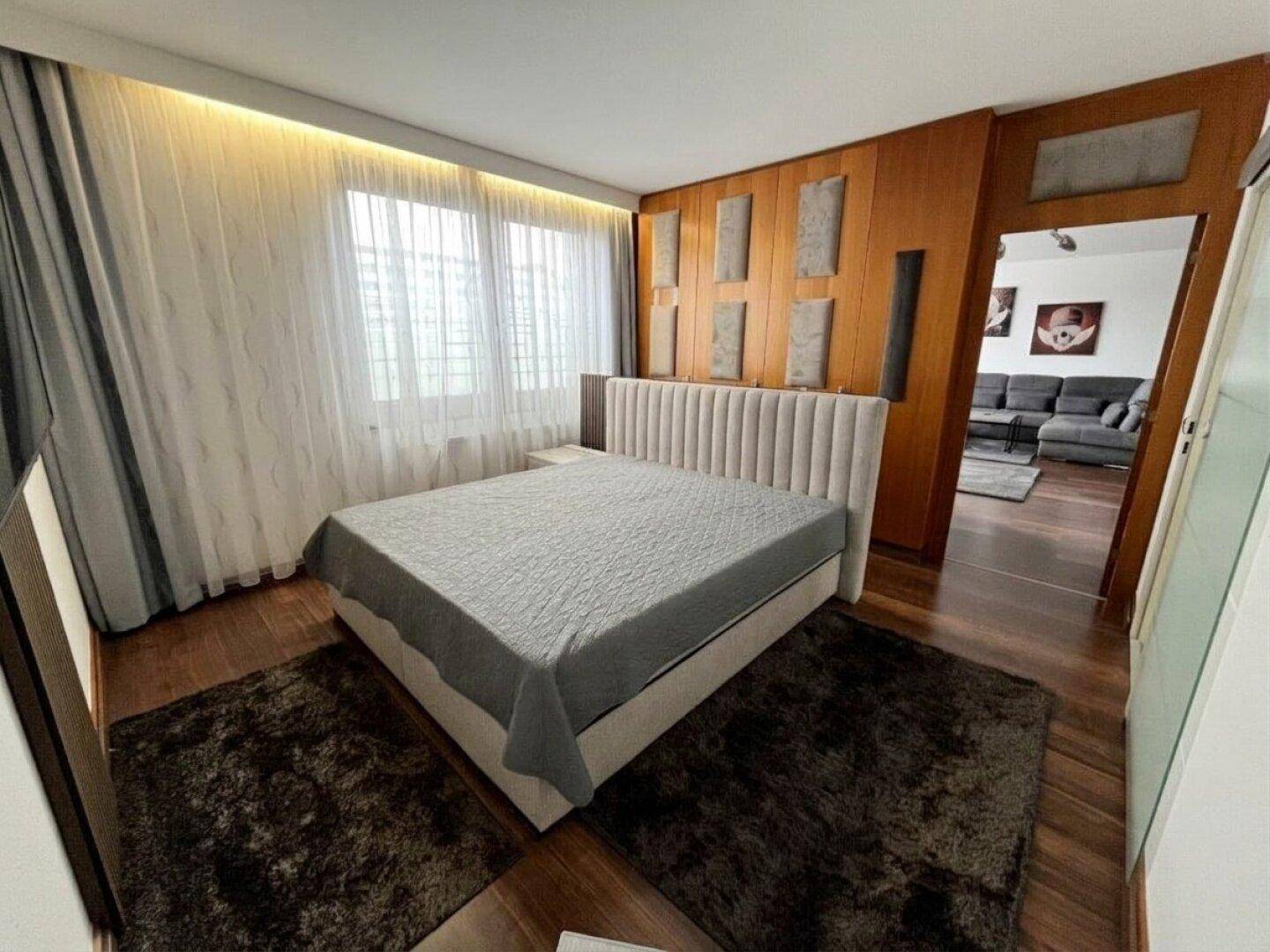 Gemütliches Schlafzimmer mit großem Bett, Holzboden und Vorhängen am Fenster.