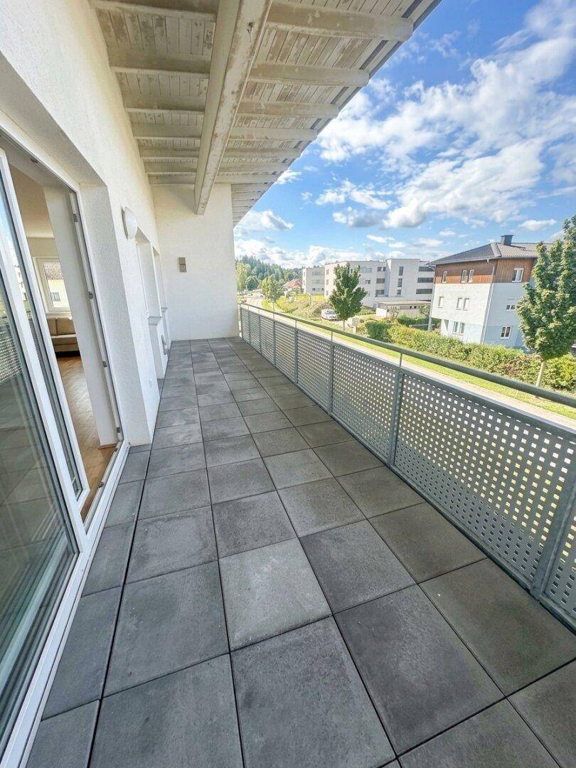 Geräumiger Balkon mit grauen Fliesen und Metallgeländer, bietet einen Blick auf die Umgebung.