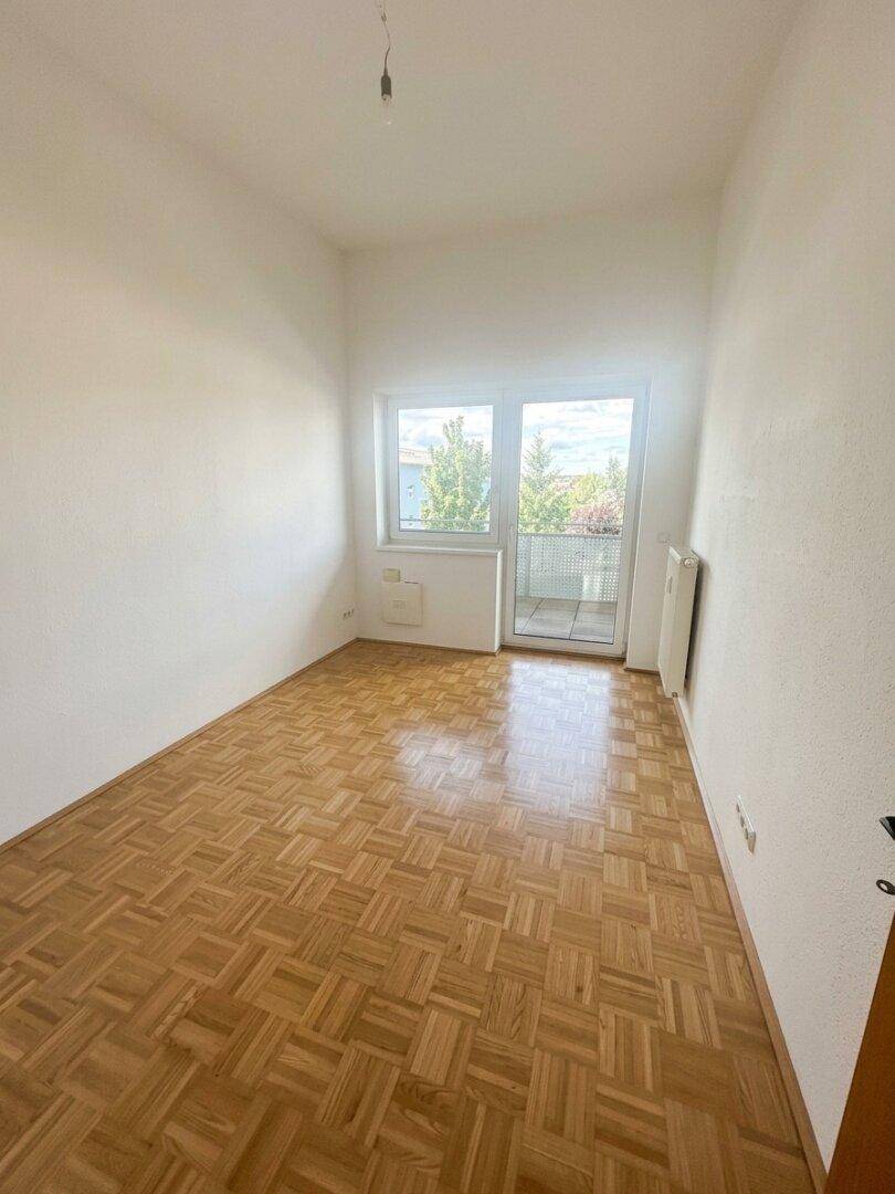 Gemütliches Zimmer mit Parkettboden und Zugang zu einem kleinen Balkon oder einer Loggia.