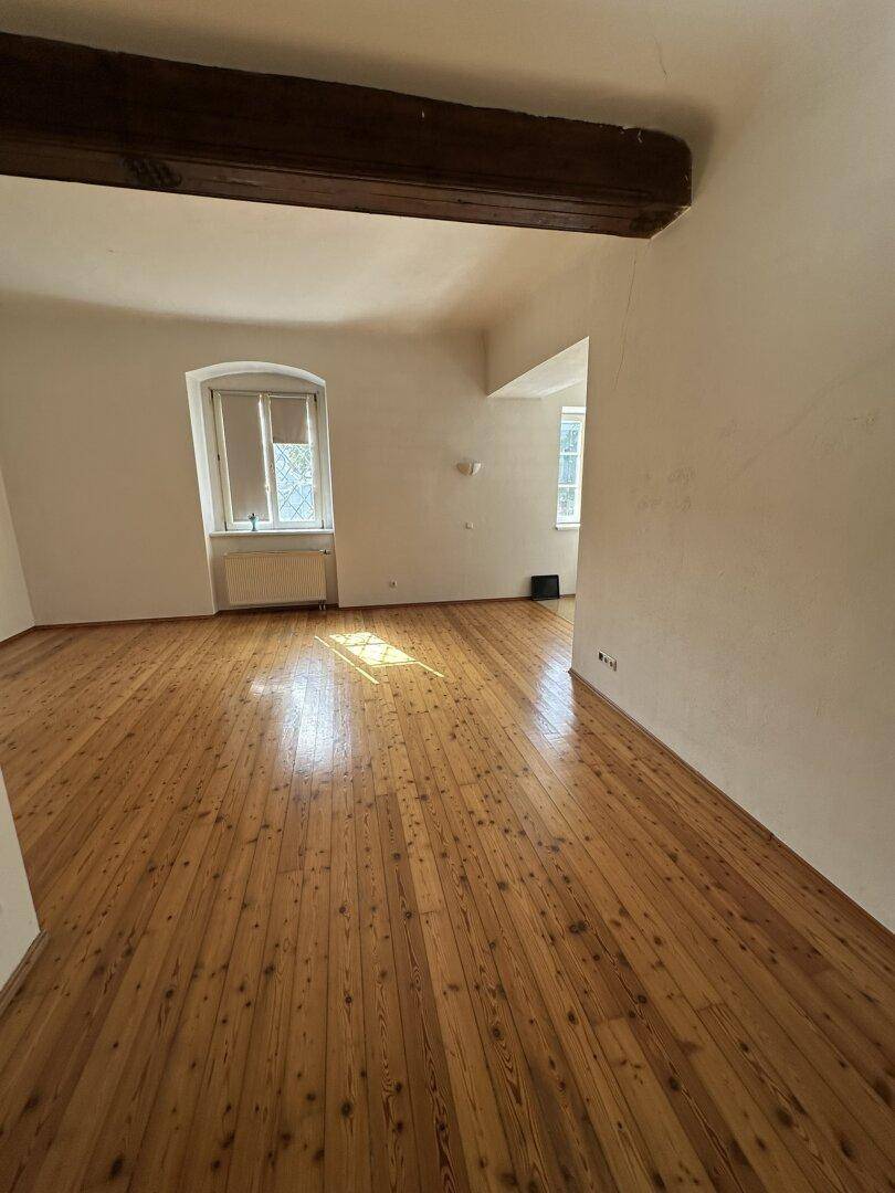 Geräumiger Wohnbereich mit warmem Holzdielenboden und natürlichem Lichteinfall durch das Fenster.