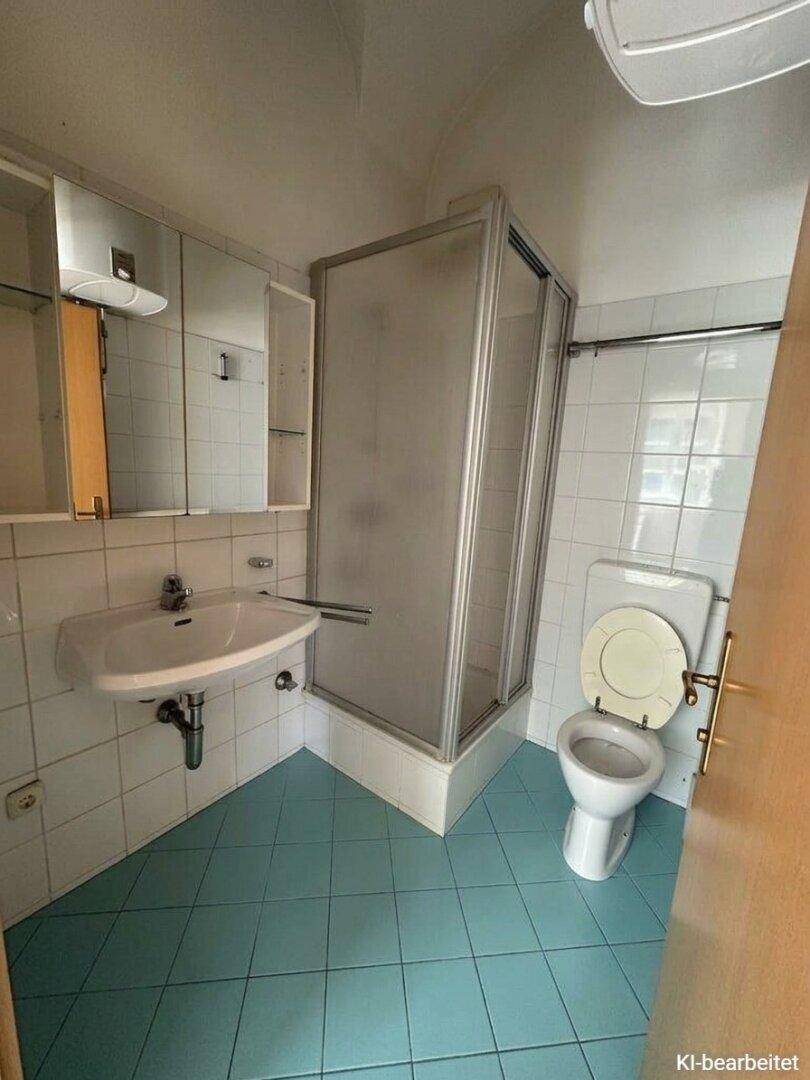 Funktionales Badezimmer mit Duschkabine, WC, Waschbecken und hellblauen Bodenfliesen.