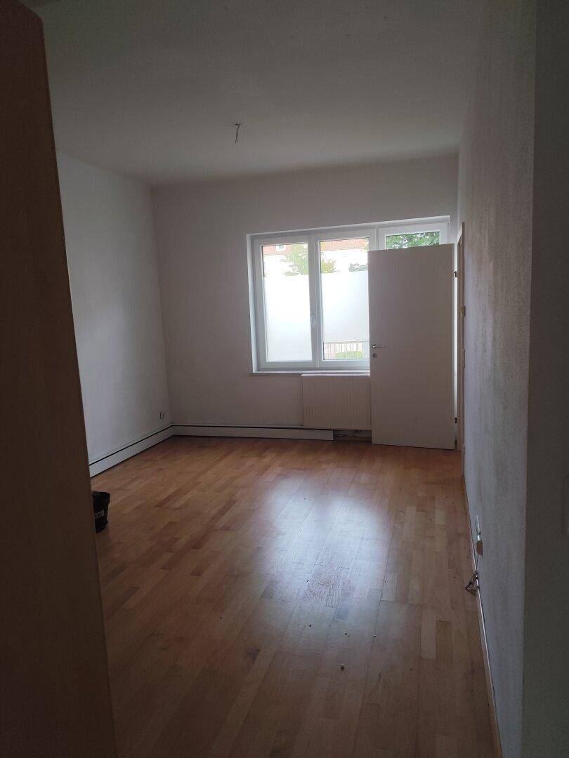 Leeres Schlafzimmer mit hellem Parkettboden und Fenster, das viel Tageslicht hereinlässt.