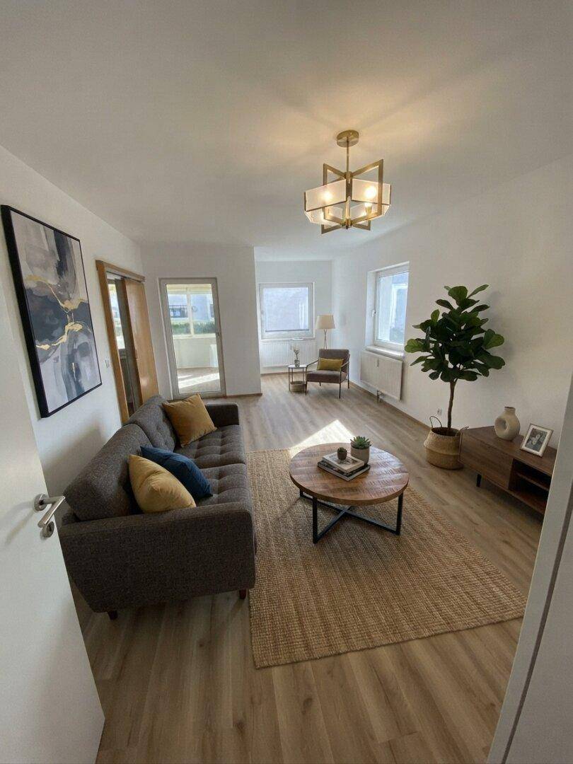 Gemütliches Wohnzimmer mit Sofa, Couchtisch, Teppich und Zugang zum Balkon, KI-bearbeitet.