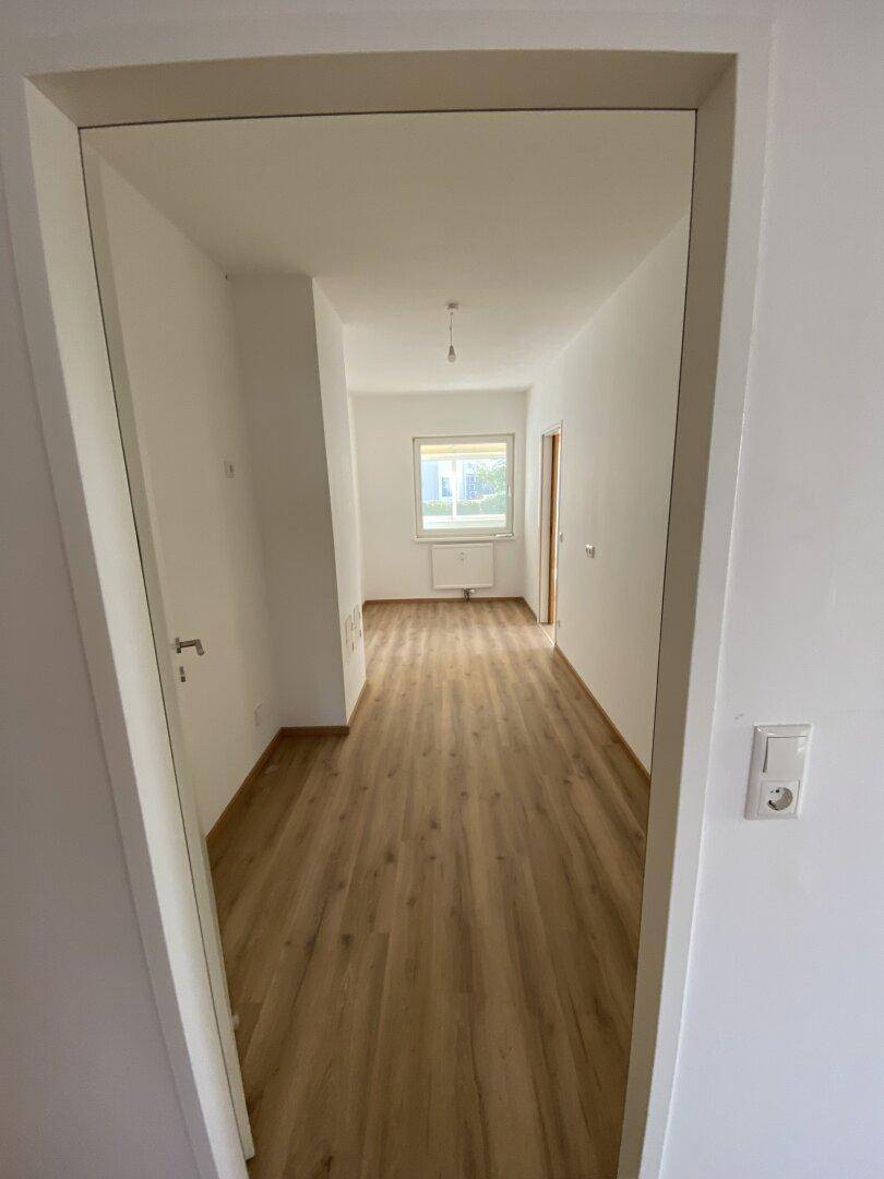Leerer Raum mit Laminatboden und Fenster, bereit zur individuellen Gestaltung.