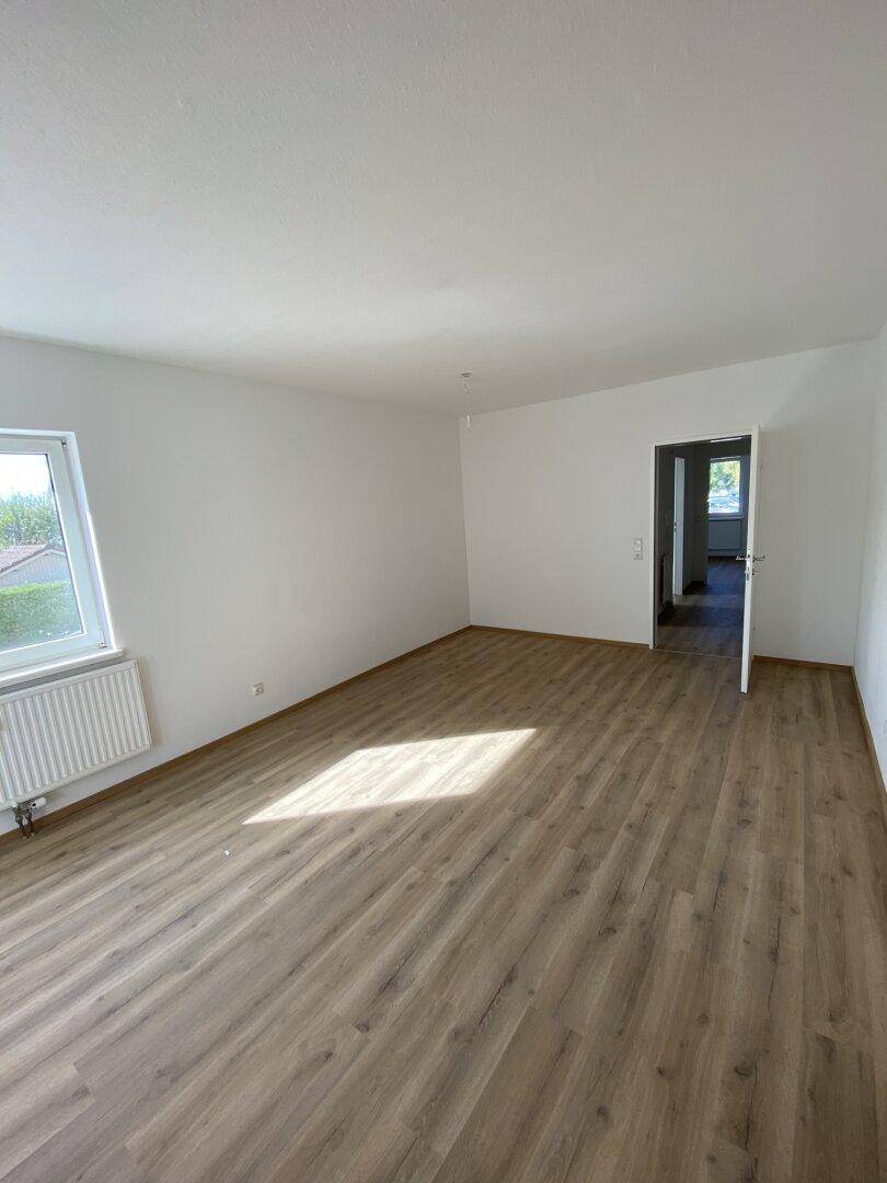 Leerer Wohnraum mit Laminatboden und großem Fenster, ideal für individuelle Einrichtung.