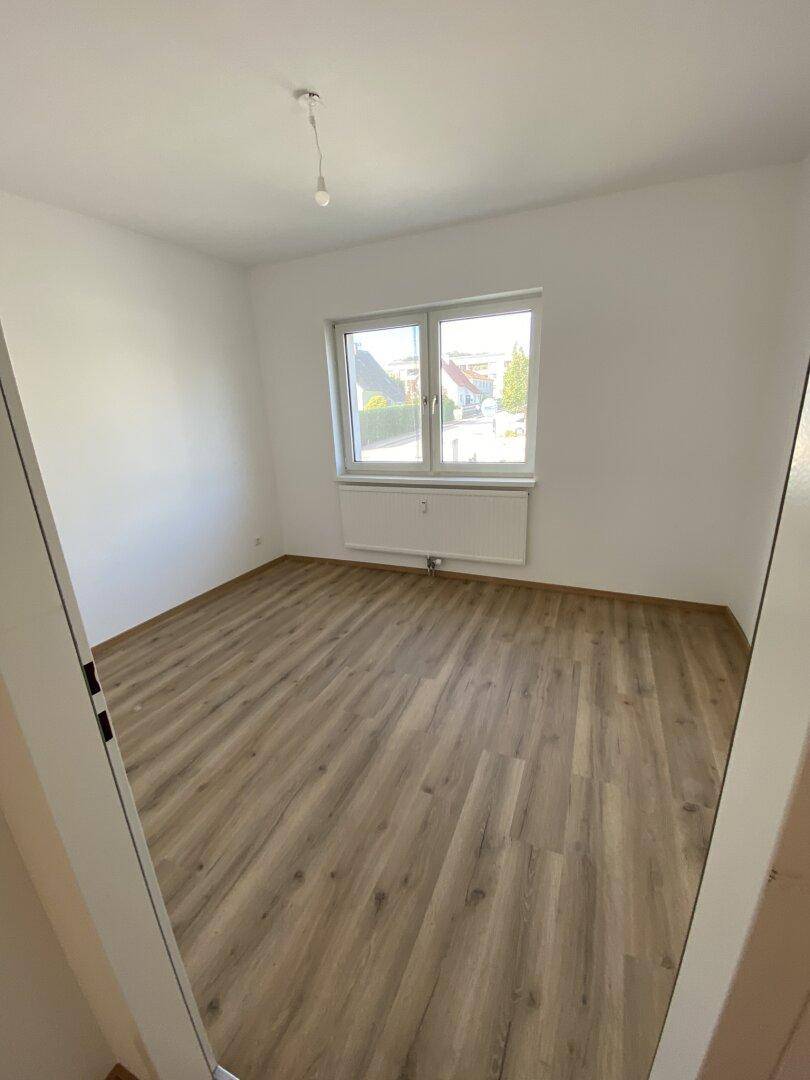 Leeres Schlafzimmer mit Laminatboden und großem Fenster, bereit zur Einrichtung.