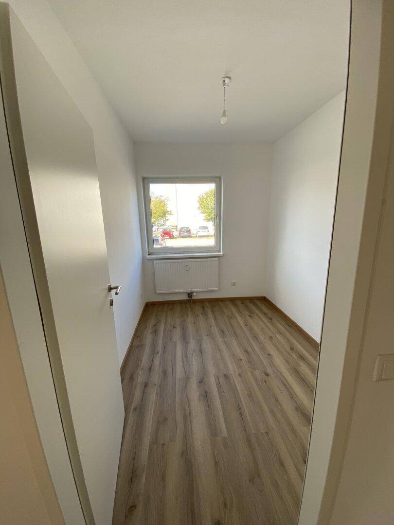 Leerer Raum mit Laminatboden und Fenster, vielseitig nutzbar.
