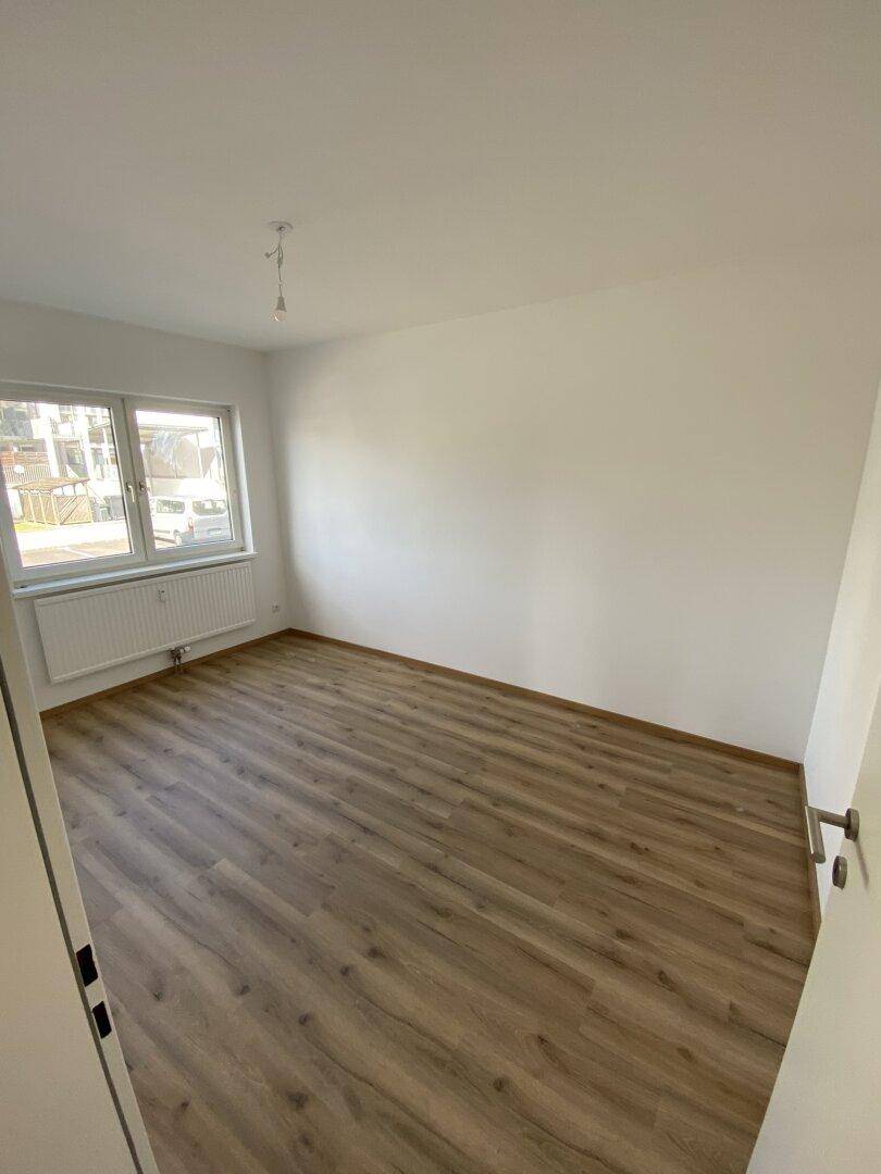 Leerer Raum mit Laminatboden und Fenster, ideal für Schlaf- oder Arbeitszimmer.