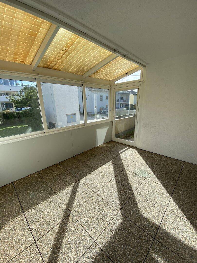 Heller, verglaster Balkon mit Fliesenboden und viel Tageslicht.