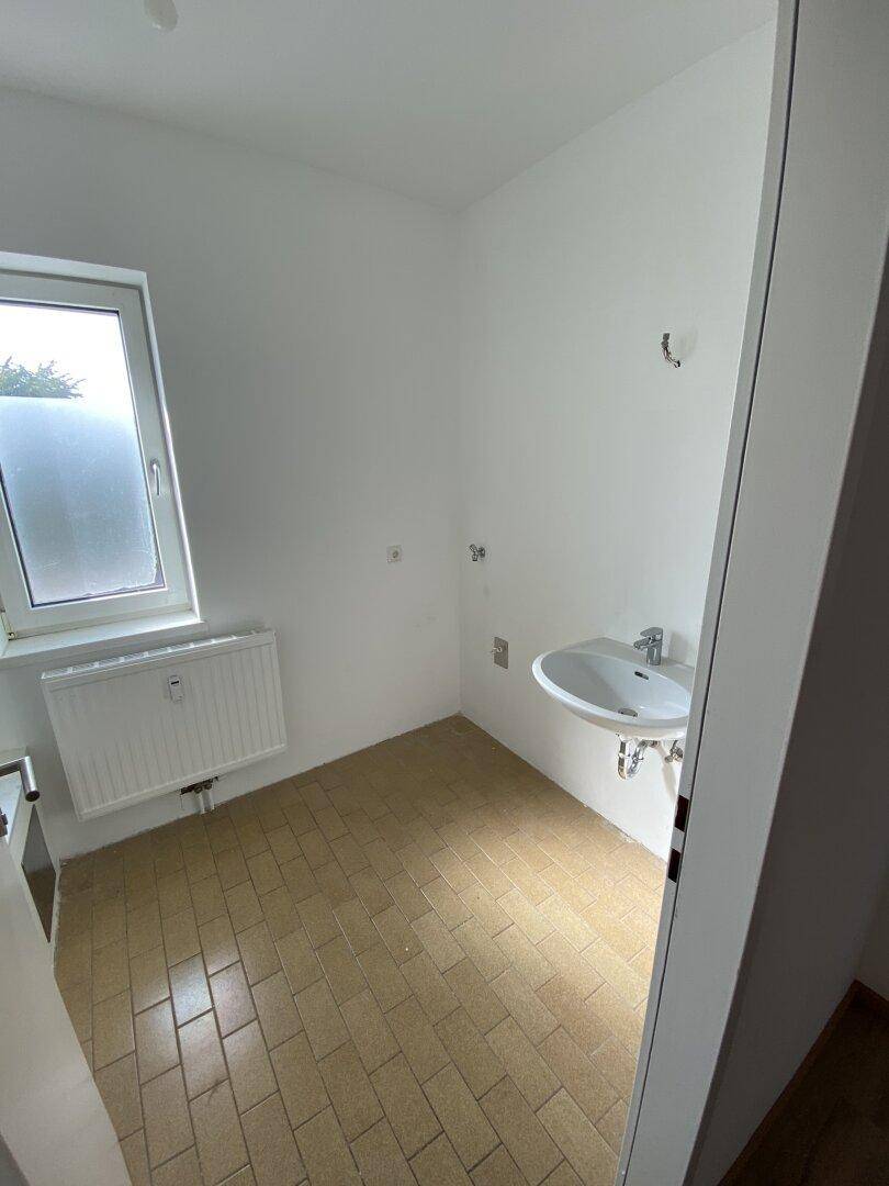 Leerer Raum mit Waschbecken, Fenster und Fliesenboden, vielseitig nutzbar.