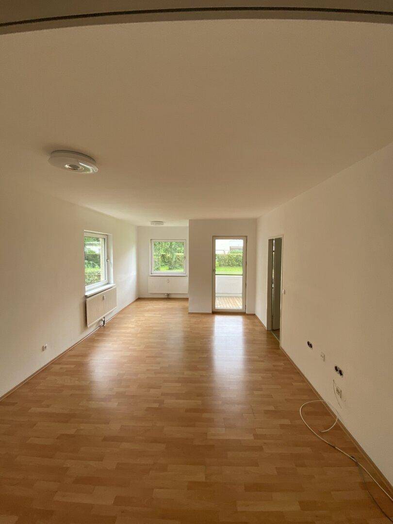 Geräumiger, leerer Wohn-Essbereich mit Parkettboden und Zugang zum Balkon.