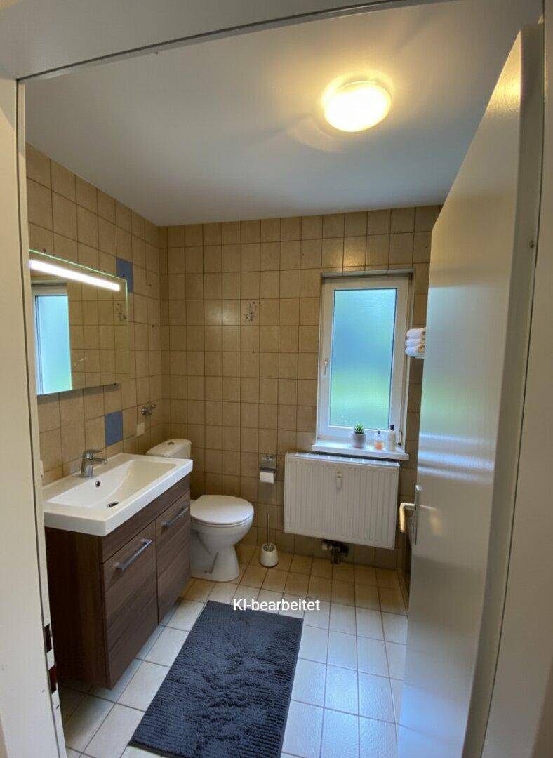 Badezimmer mit modernisiertem Waschtisch, WC und beigen Fliesen.